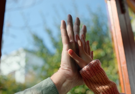 parents and daughters hands touch through glass